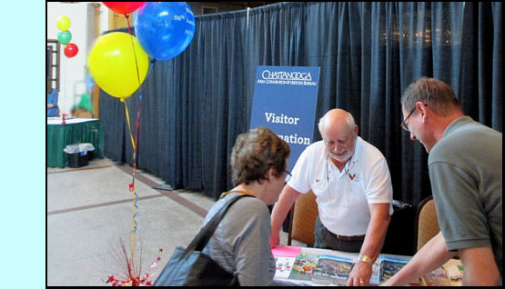 Two pictures show a man behind a small table showing people maps and brochures.  One photo has a man with two children, the other has a man and a woman looking at the map. 